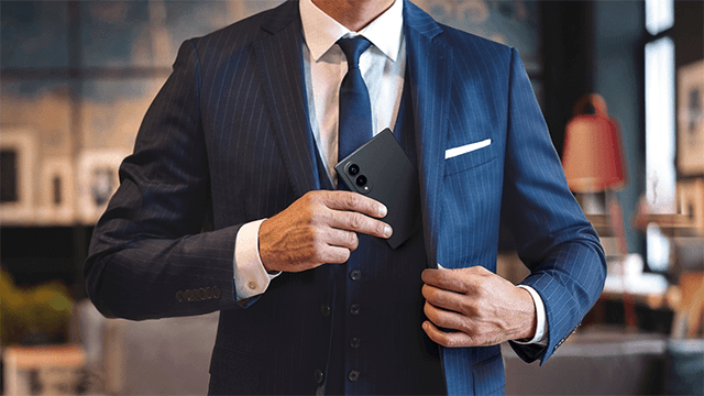 Eleganter Geschäftsmann in Anzug, der ein Smartphone aus der Innentasche seines Sakkos holt, symbolisiert moderne Kommunikation.